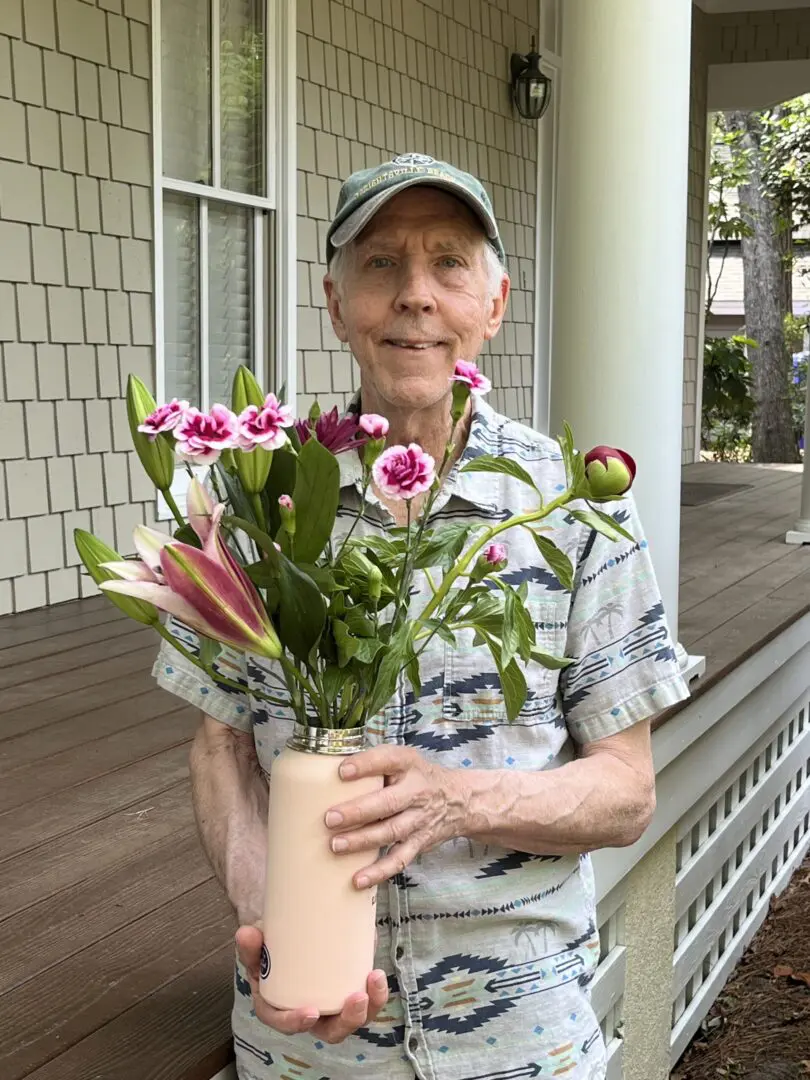 A man holding a flower pot on the porch of his home.