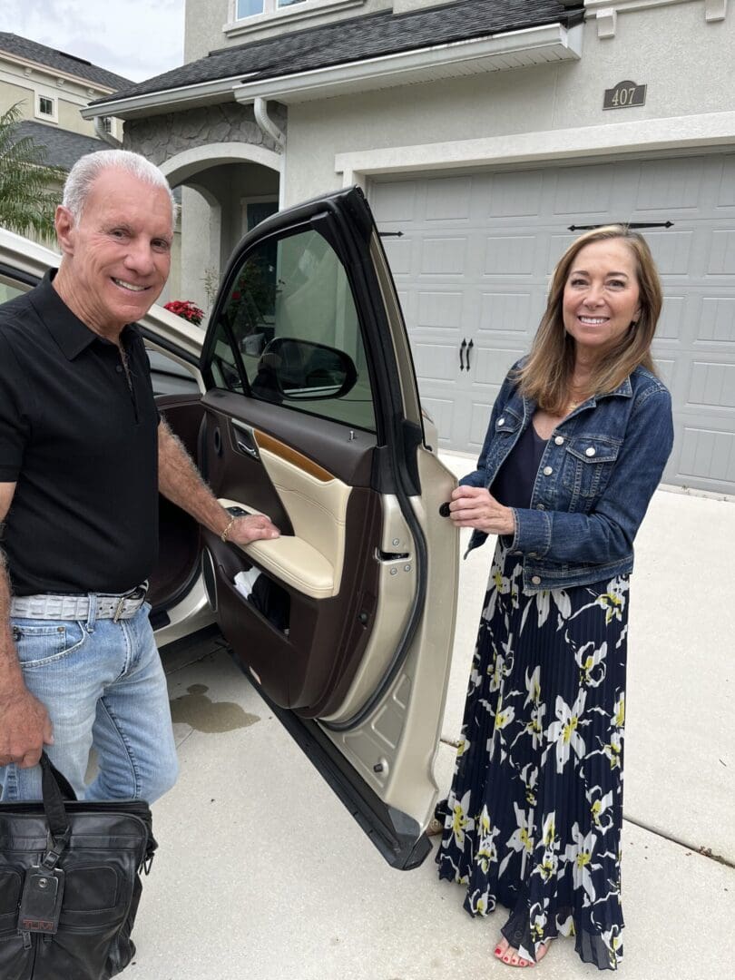 A man and woman standing next to the door of their car.